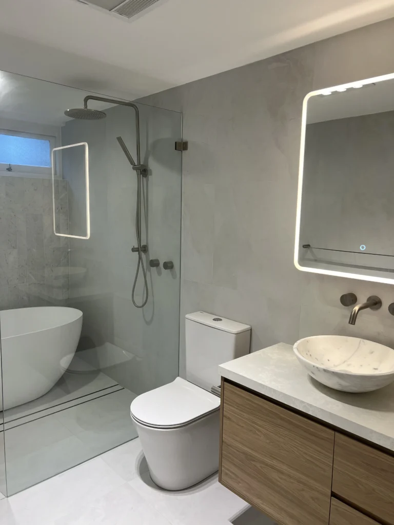 NF Build modern bathroom renovation featuring freestanding tub, walk-in shower, wooden vanity, and illuminated mirror