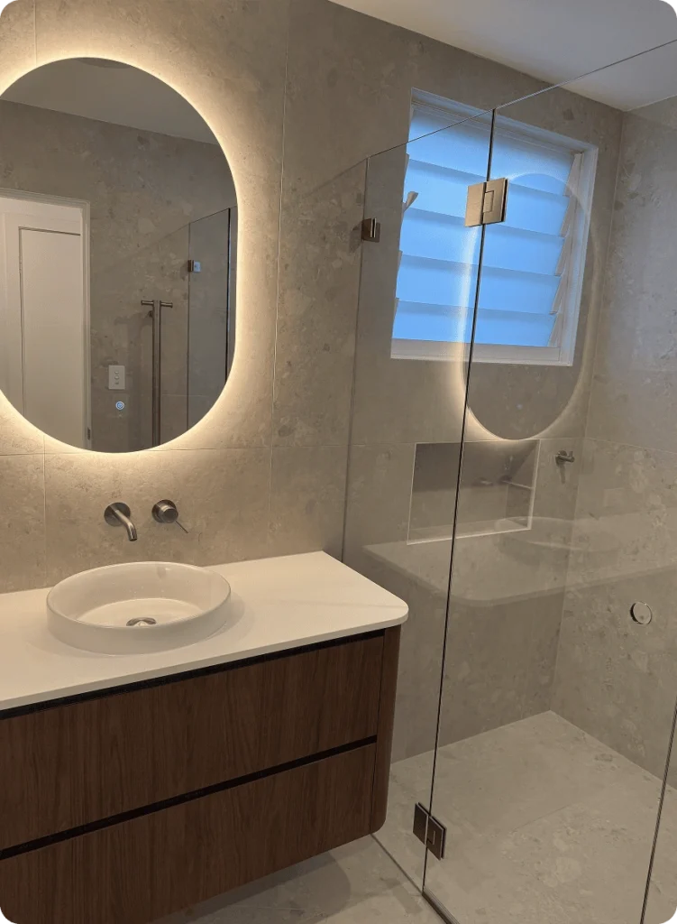 NF Build modern bathroom featuring illuminated oval mirror, floating timber vanity, and walk-in glass shower