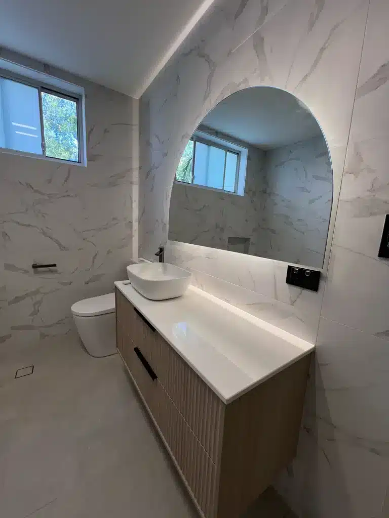 Modern bathroom renovation with wooden vanity, vessel sink, and illuminated mirror