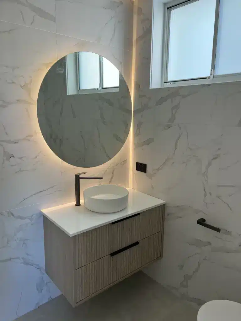Wall-hung wooden bathroom vanity with round illuminated mirror and vessel sink