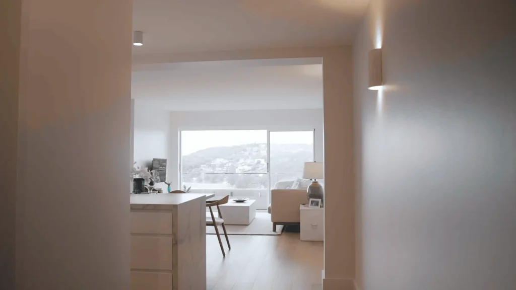 Modern interior view looking into a bright living room and kitchen island with large sliding glass doors overlooking a scenic hillside view.