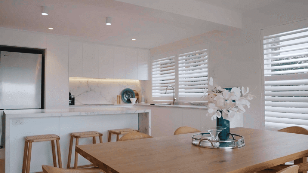 NF Build open plan kitchen and dining room with modern white cabinetry, island bench, and wooden dining table