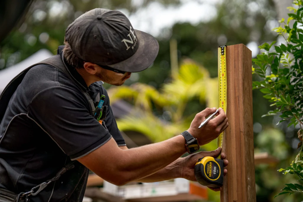 NF Build carpenter measuring timber post with tape measure on construction site