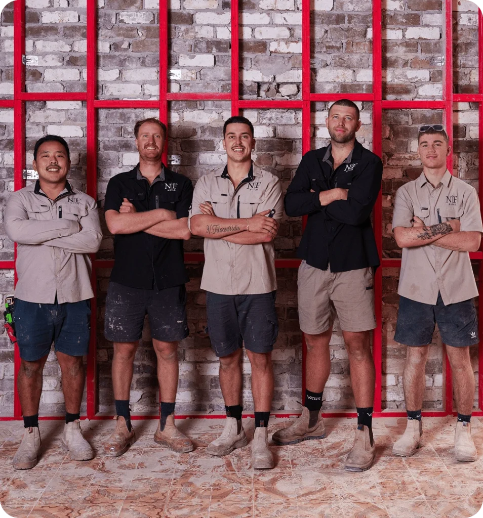 NF Build construction team posing in front of brick wall and red steel framing