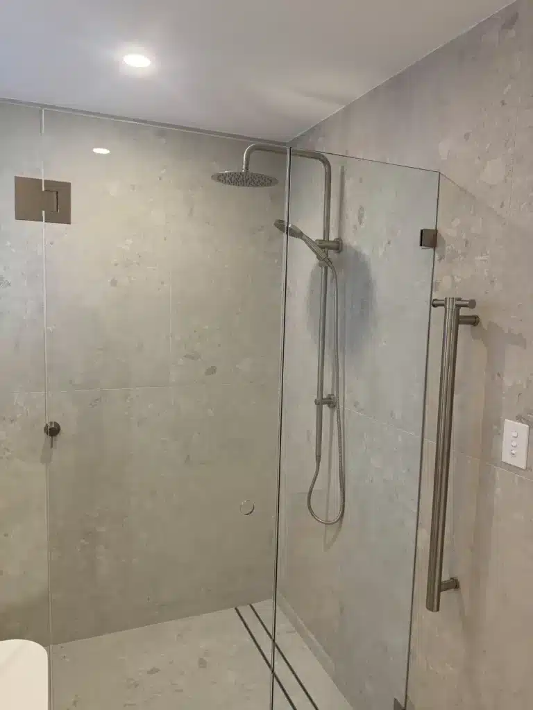 Modern walk-in glass shower with overhead shower head and grey wall tiles